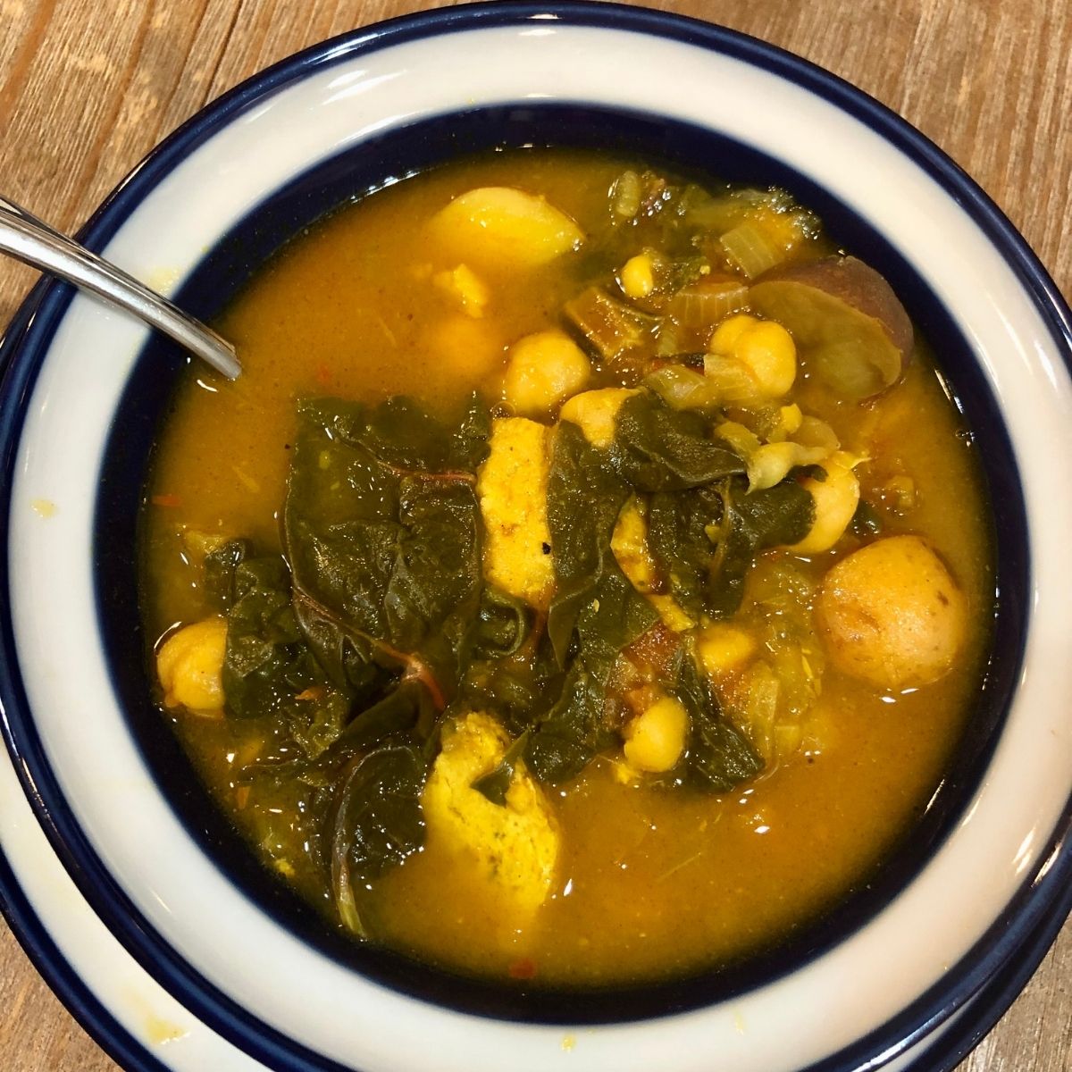 Weight Watchers Swiss chard and Potato soup in a white bowl with a blue stripe on a wooden table