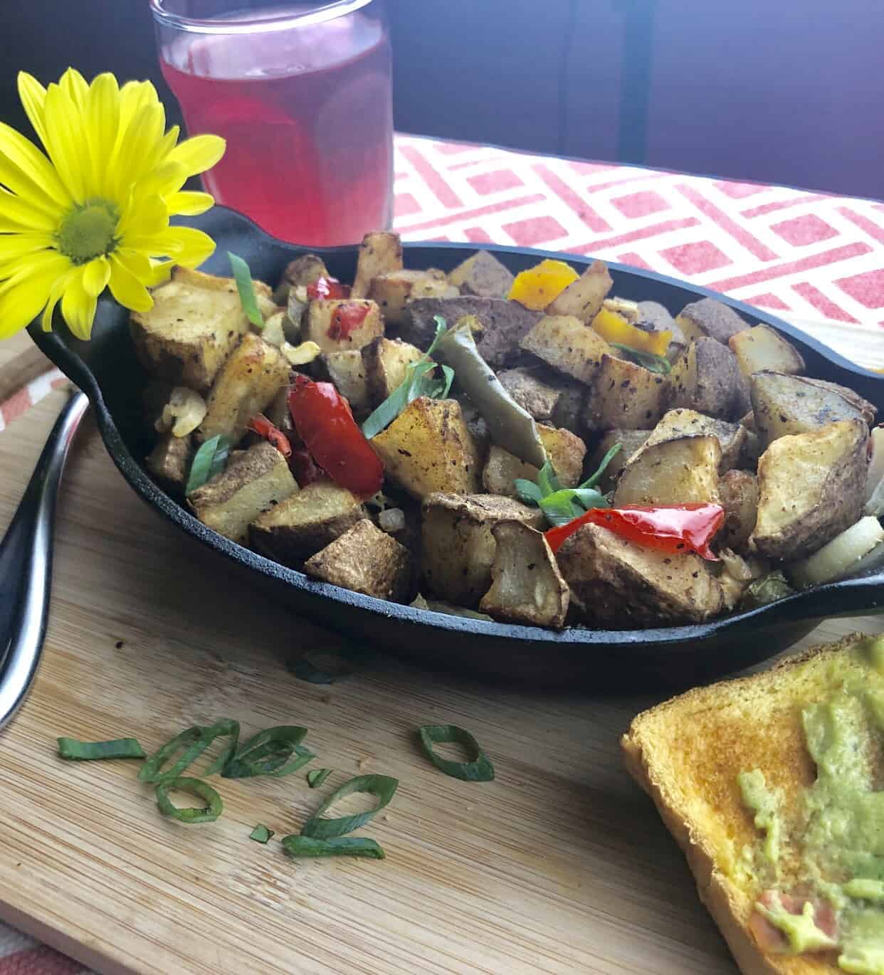 Healthy Home Fried Potatoes in a black casserole dish with cur chives and avocado toast on a wooden cutting board