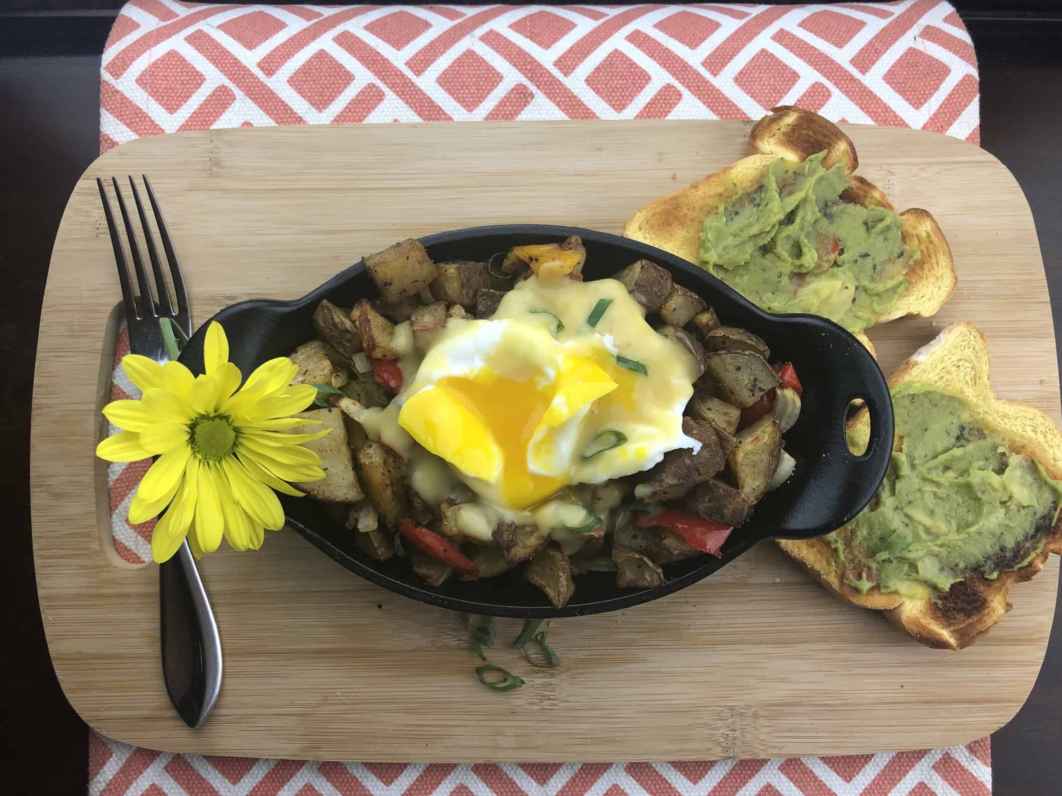 Air Fried Home Fries with a poached egg on top in a black casserole dish with a fork and avocado toast on a wooden cutting board