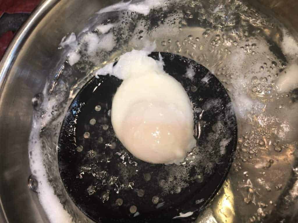 A Poached Egg being lifted out of a pot of boiling water with a black strainer spoon
