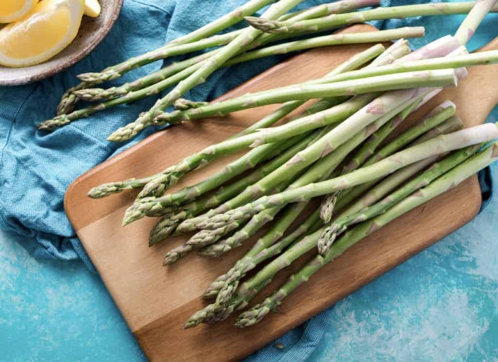 Fresh Green Asparagus on a wooden cutting board with lemon wedges on a blue tablecloth