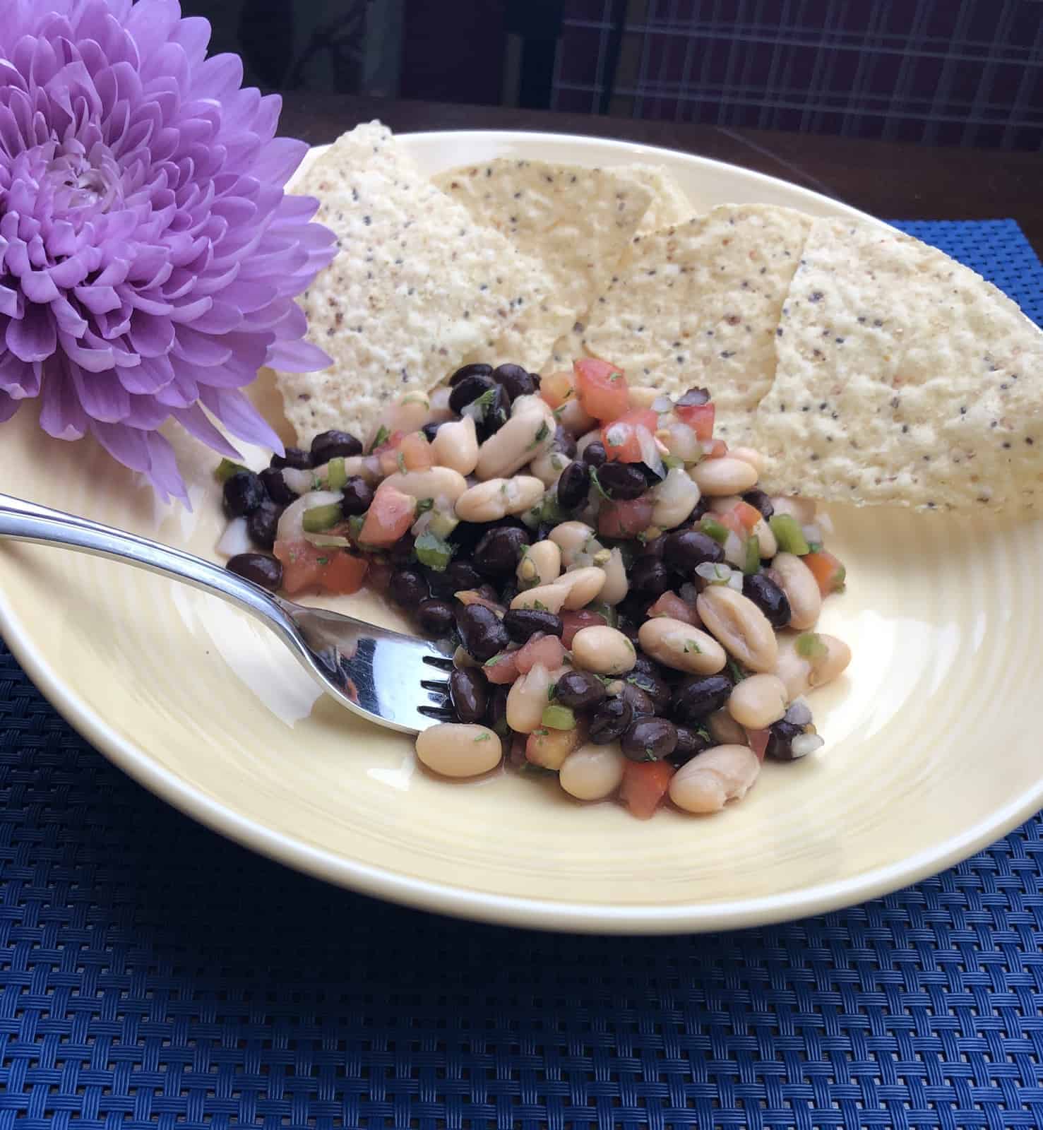  bean salad on a yellow plate with Tostito corn chips and a fork and a purple flower