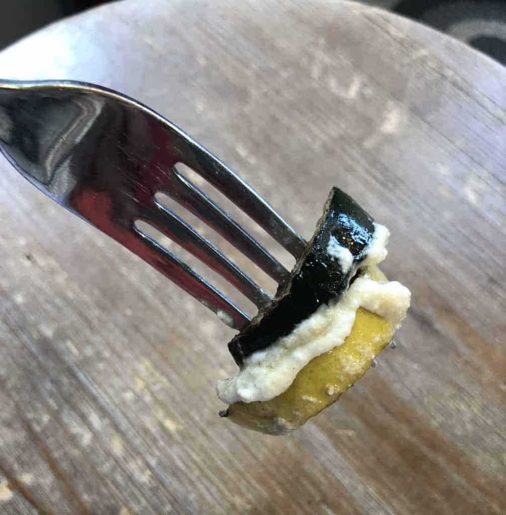 A slice of zucchini and squash with ricotta on a fork over a wooden table