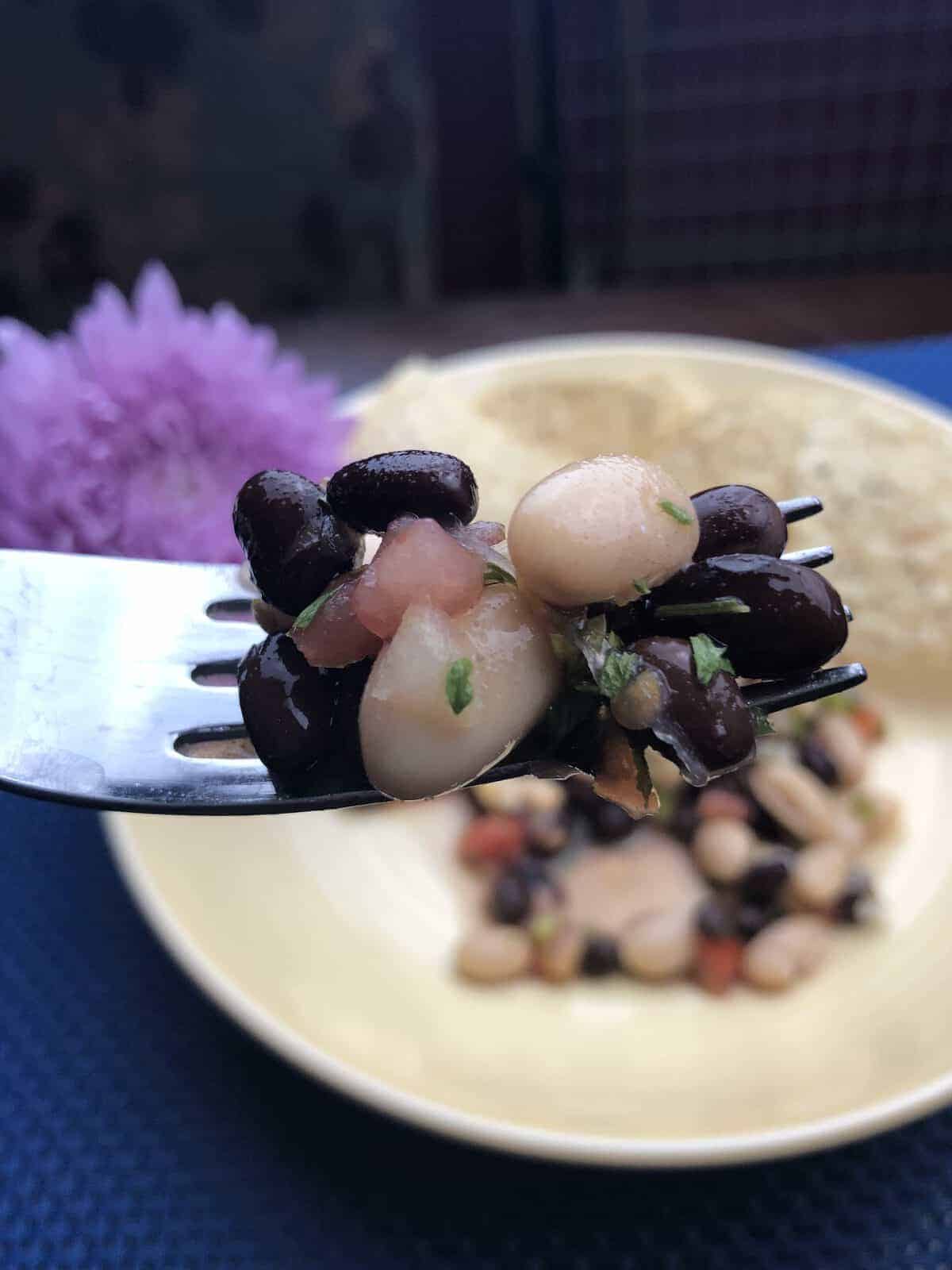  Bean salad on a fork over a bowl of bean salad with a purple flower