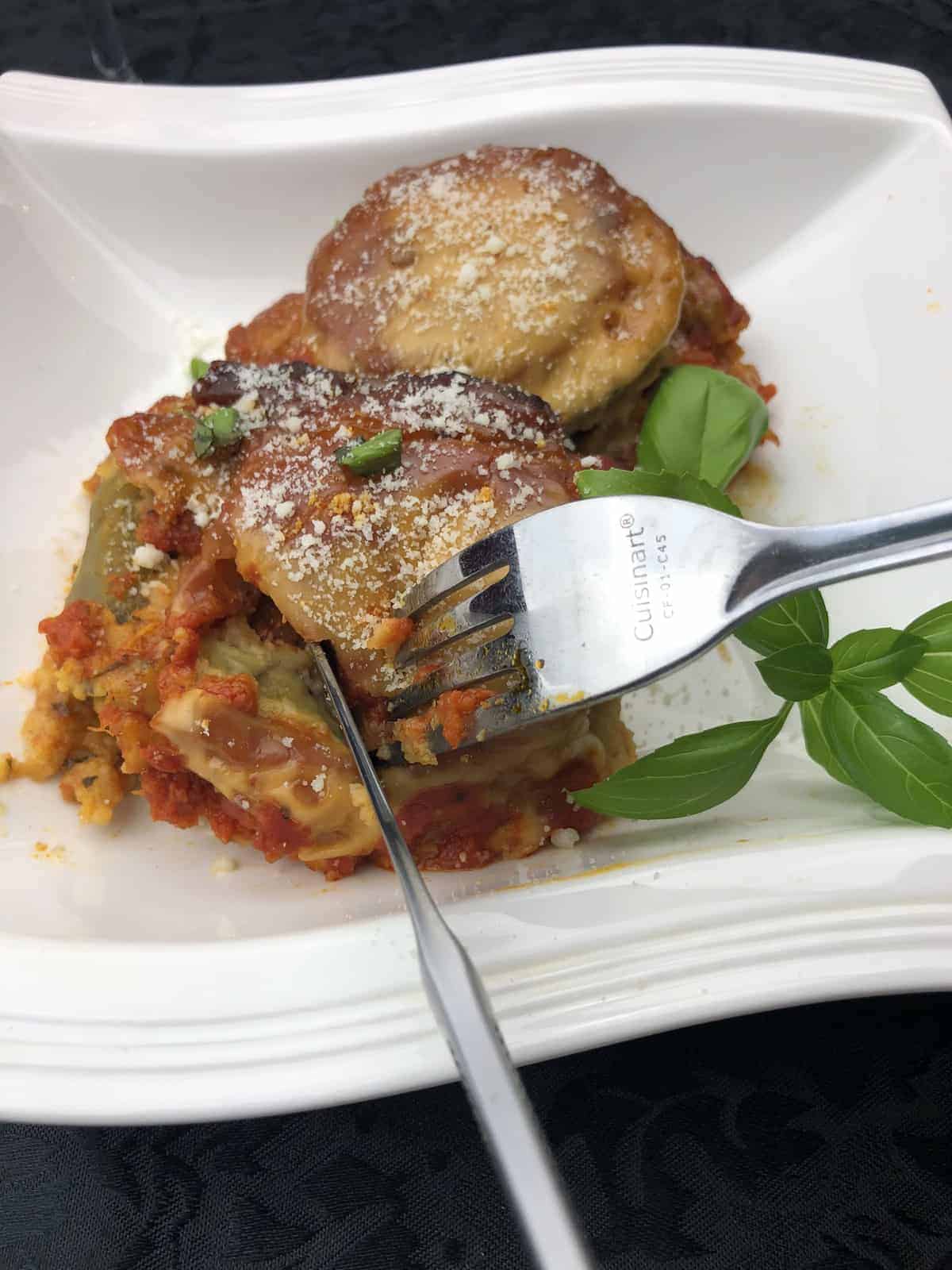 Eggplant parmigiana in a white bowl with a fork and fresh basil