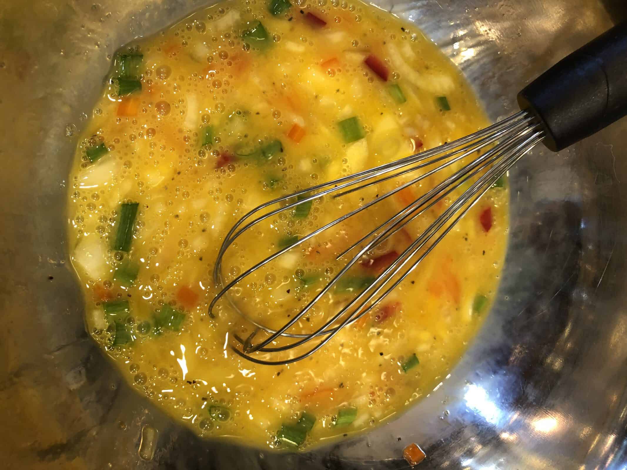 A whisk Beating the egg mixture in a stainless steel bowl