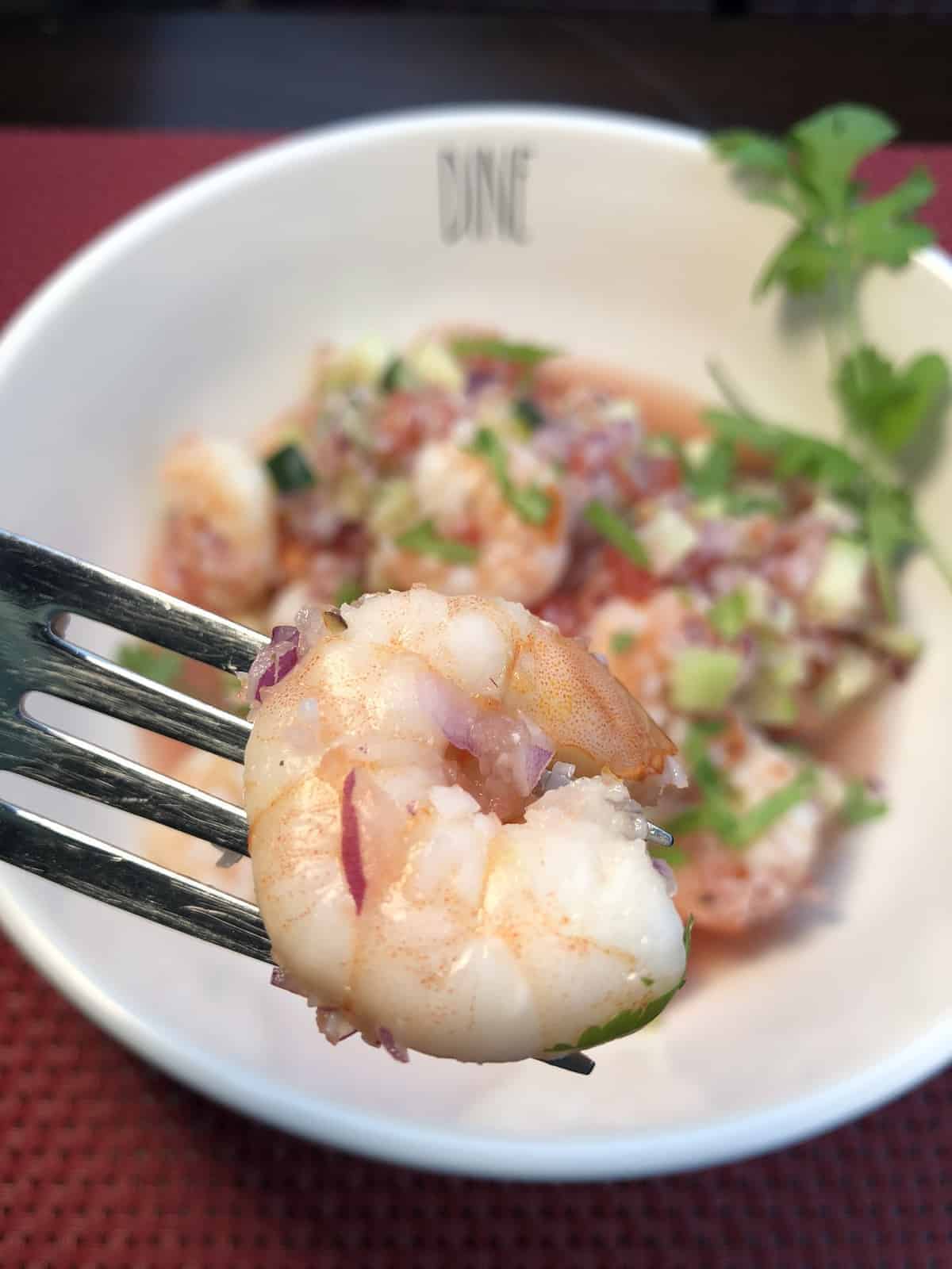 A bite of Shrimp Ceviche on a fork over a white bowl containing homemade shrimp ceviche