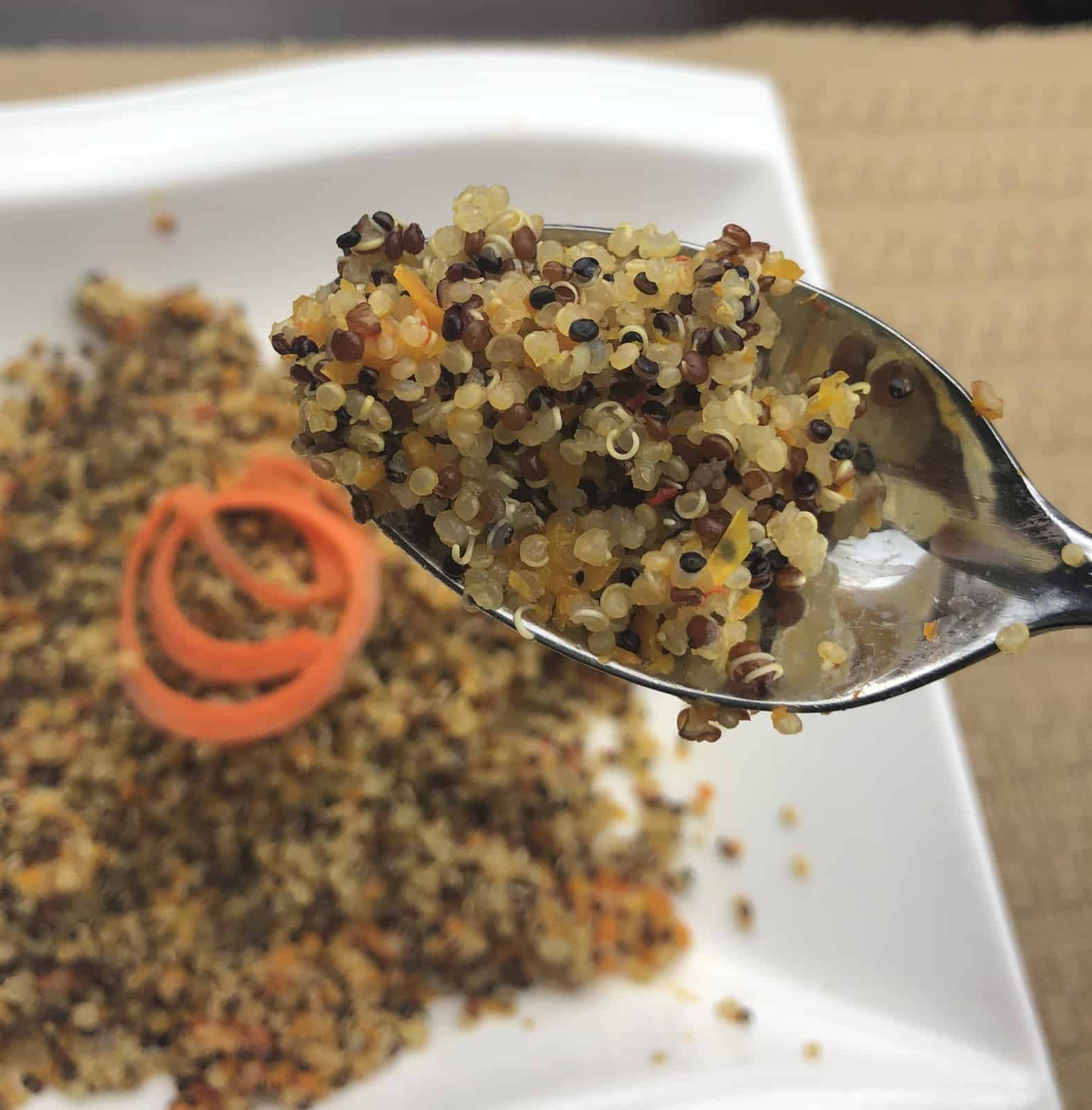 Quinoa in a spoon hovering over quinoa in a white bowl with carrot spirals