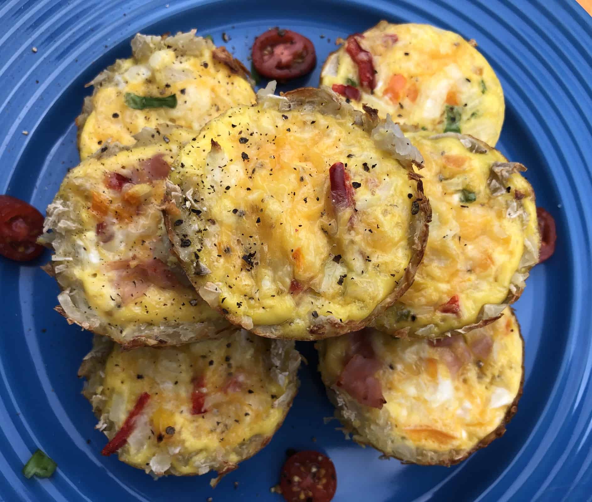 Seven mini veggie frittatas stacked on a blue plate with tomatoes