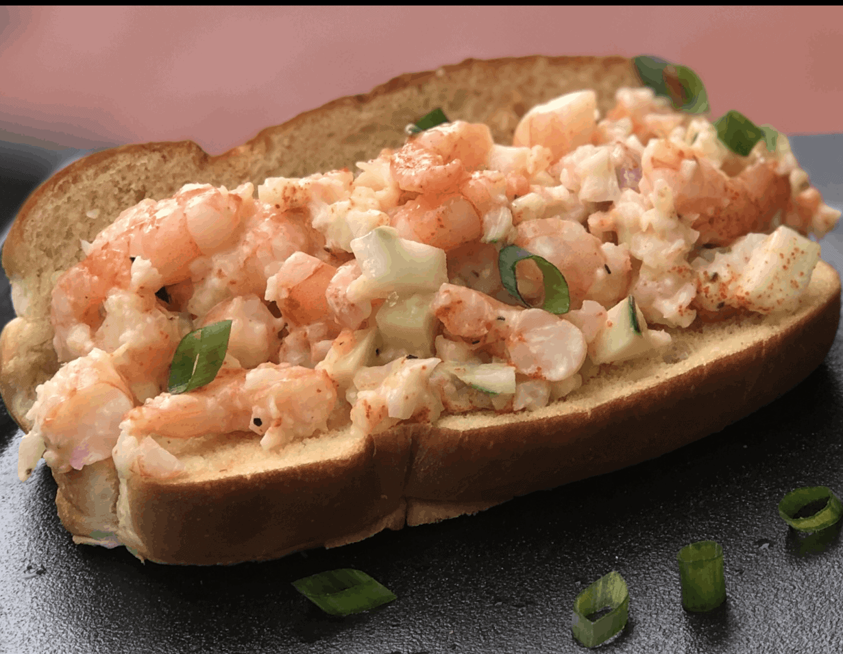Shrimp Salad with chives on a hot dog bun on a black plate