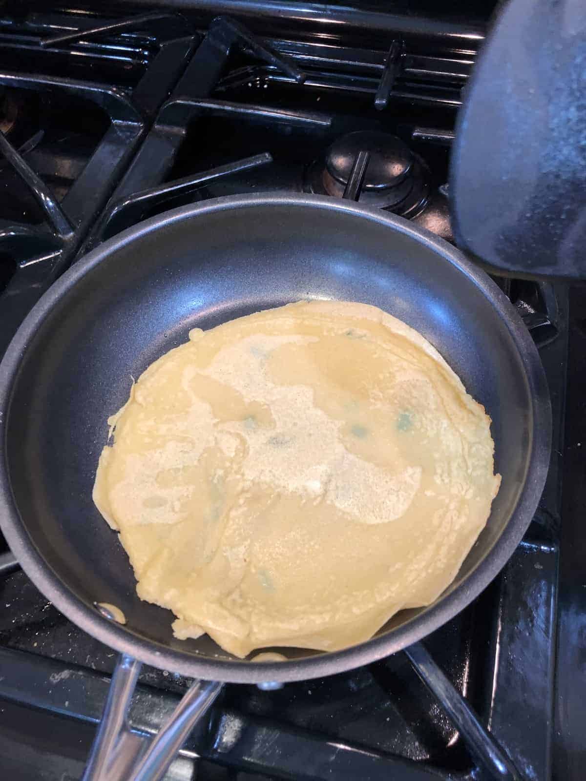 Chickpea Crepe in the pan cooking on a gas stove