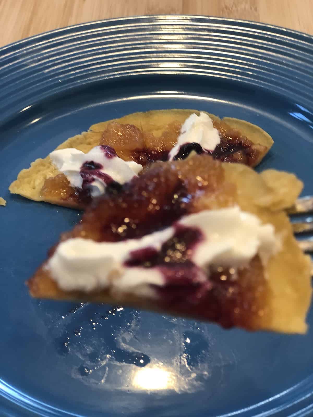 a bite of crepe with whipped cream and jelly on a fork over a blue plate