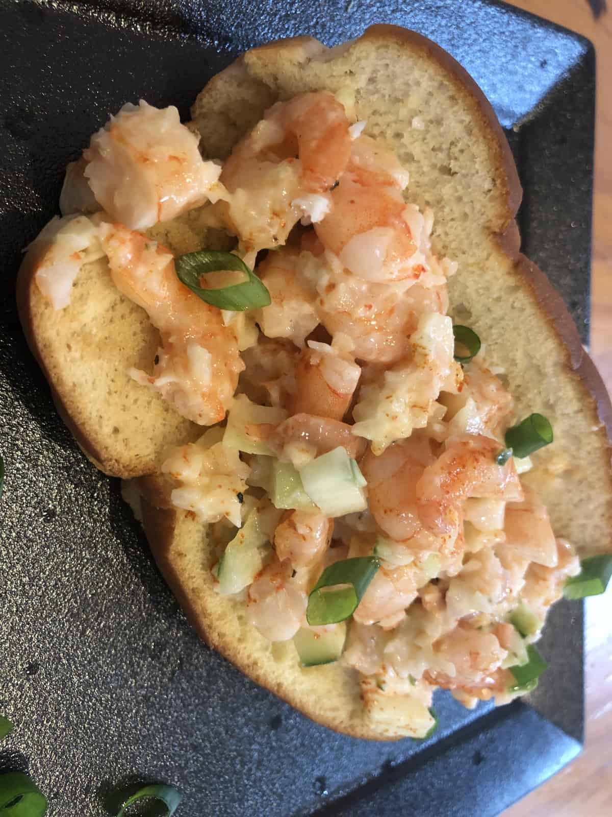 shrimp salad on a hot dog bun on a black plate