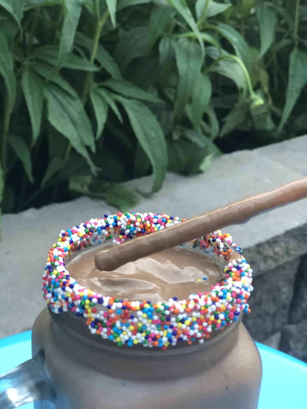 Chocolate avocado milkshake on a straw over a glass with candy sprinkles on the rim 