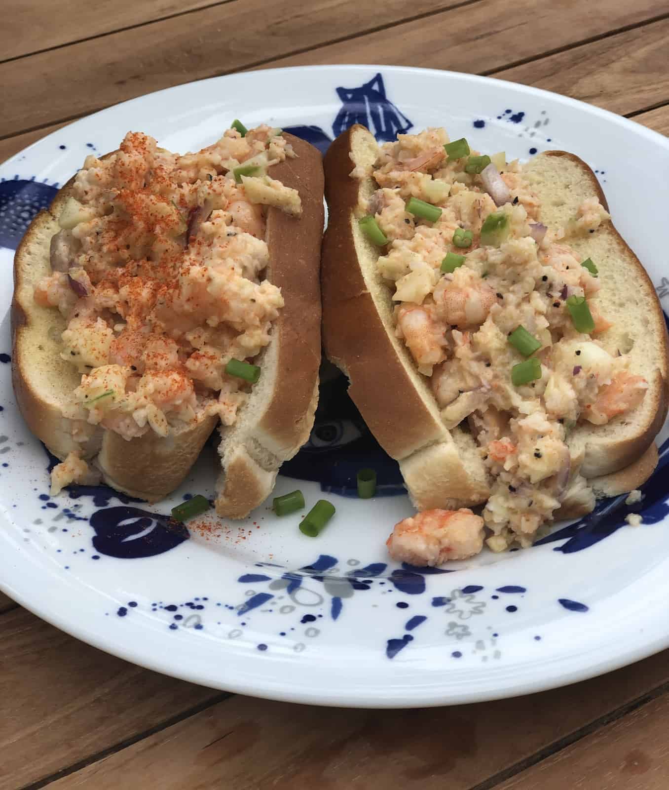 2 Shrimp Salad Sandwiches on hot dogs buns on a white and blue plate on a wooden table