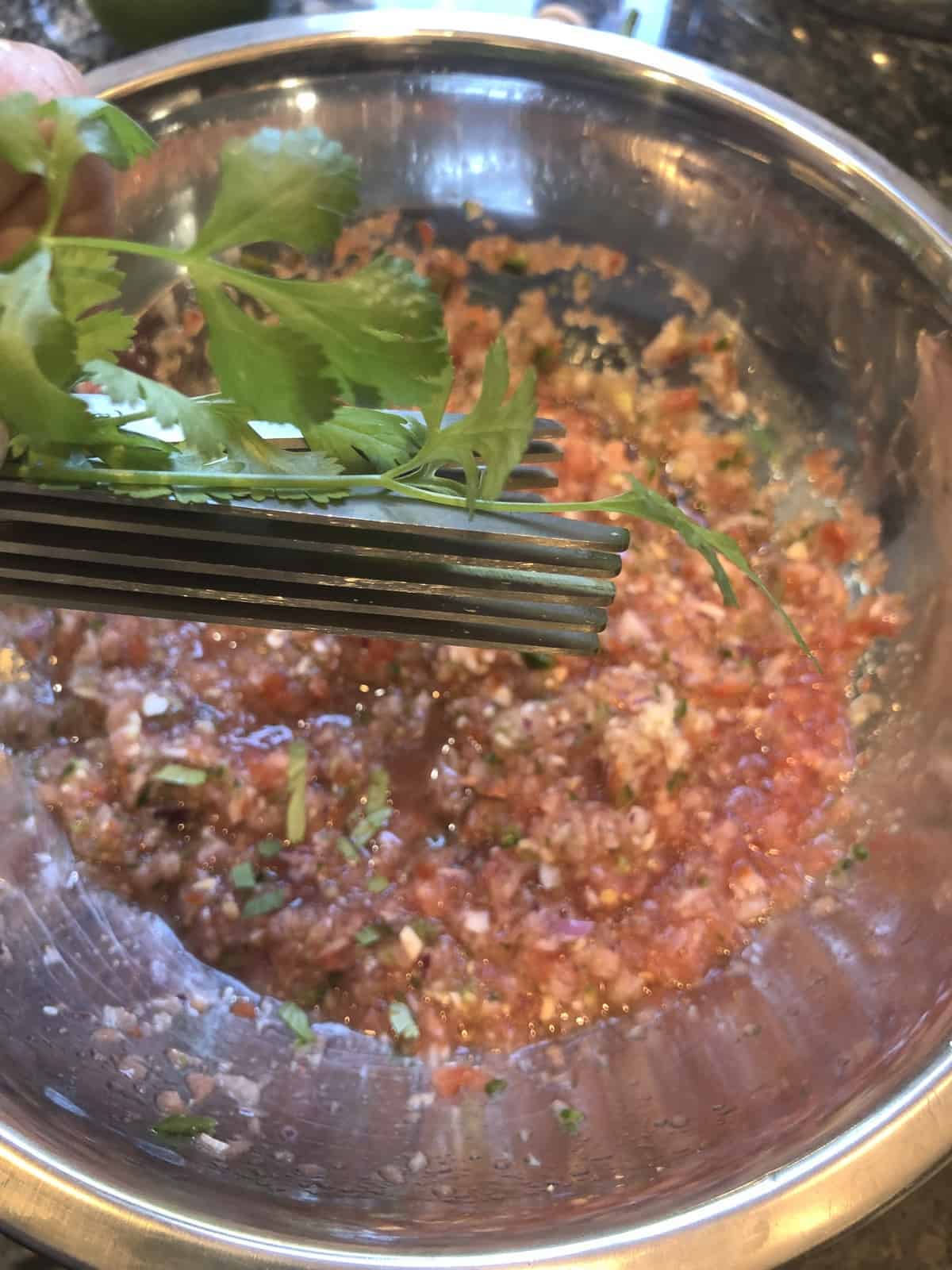 chopping fresh cilantro with herb scissors over a bowl of homemade salsa