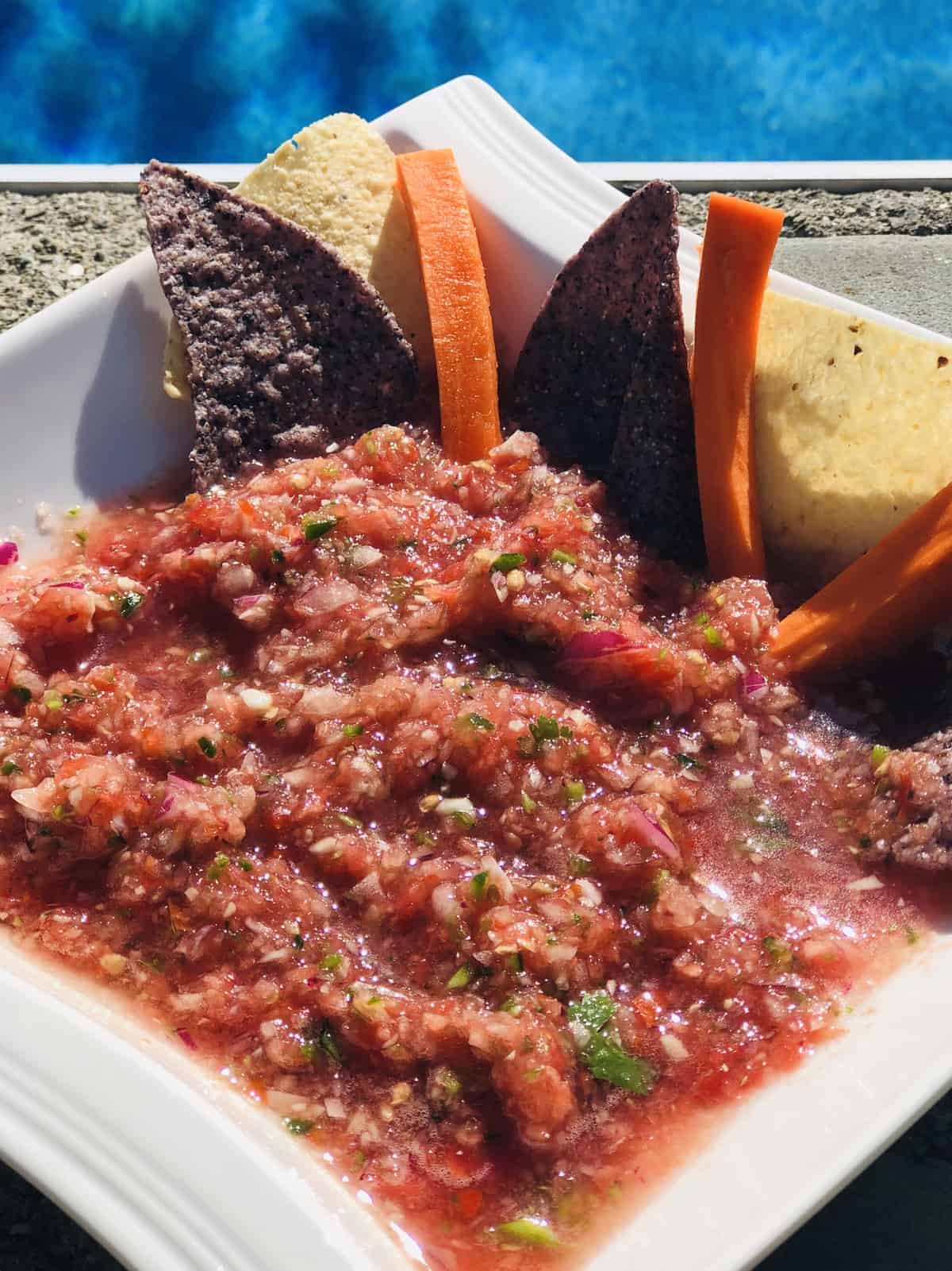 a bowl a fresh homemade salsa with yellow and blue Tostito chips and carrot sticks