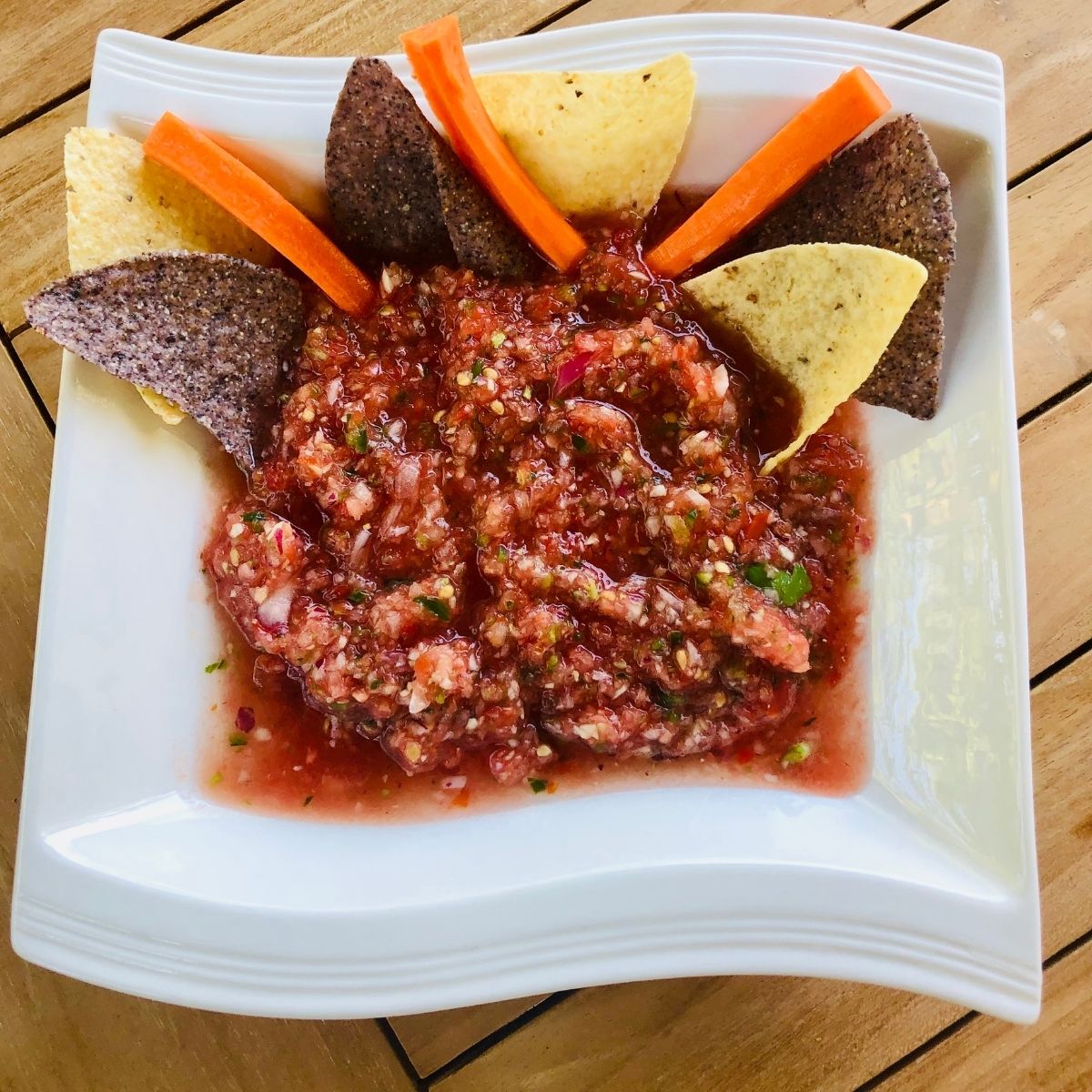 Homemade Jalapeno Salsa in a square white bowl with tortilla chips and carrot sticks on a wooden table