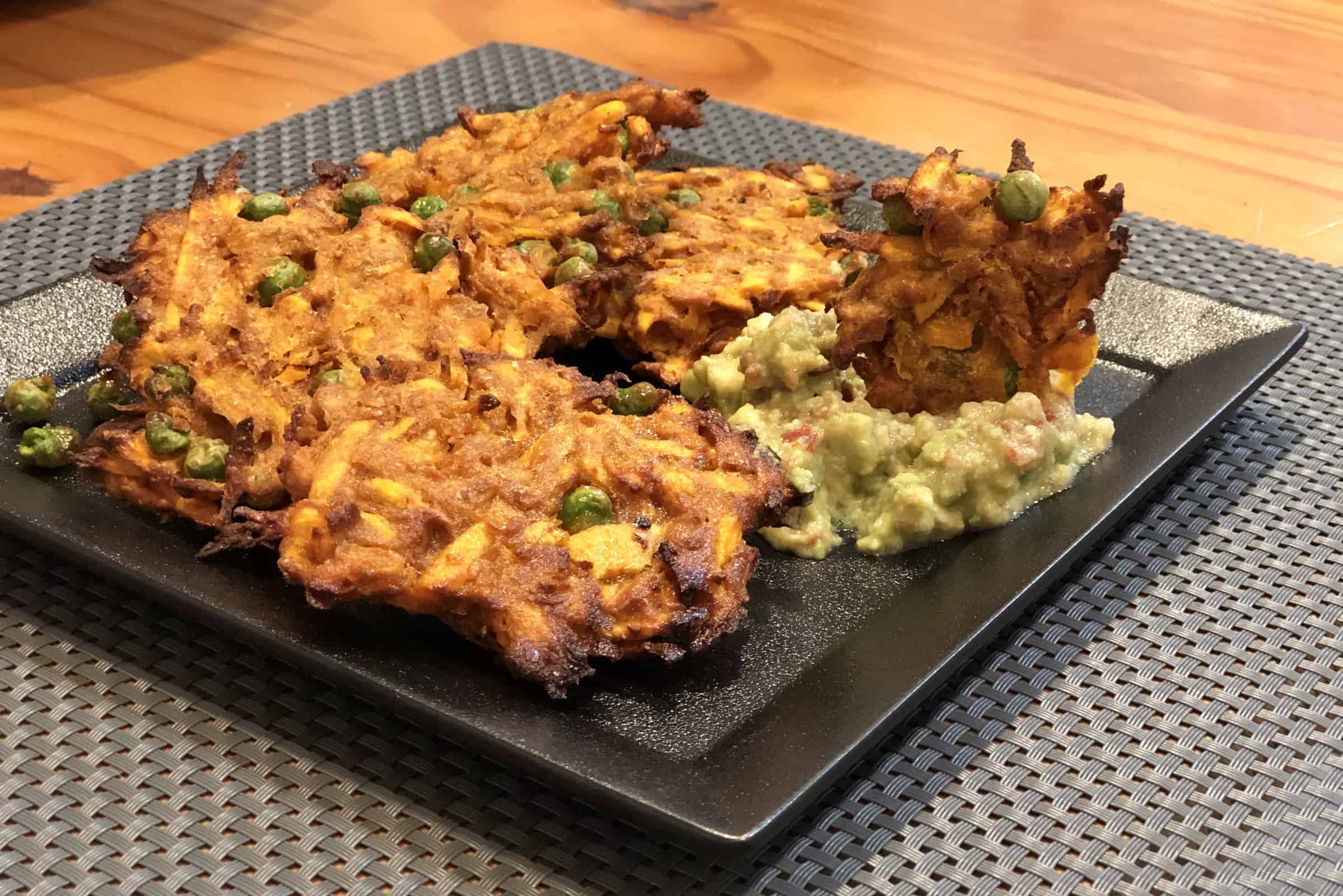 Curried Sweet Potato Fritters and guacamole on a black plate on a gray placemat on a wooden table