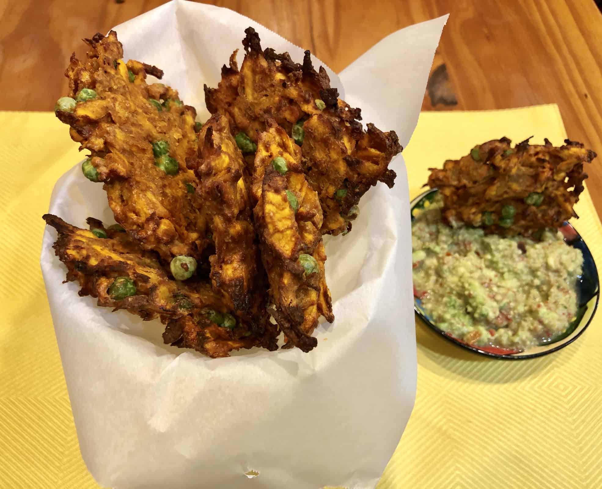 Curried Sweet Potato Fritters wrapped in parchment paper with a side of guacamole on a yellow placemat on a wooden table