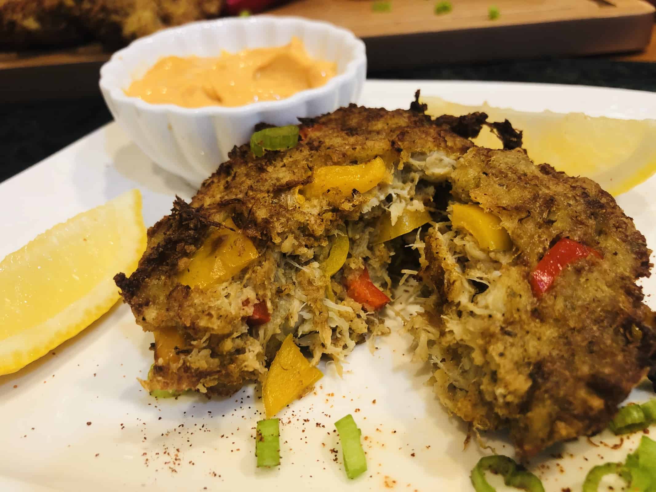 A serving of a crispy air fried crab cake on a white plate with lemon slices and dip