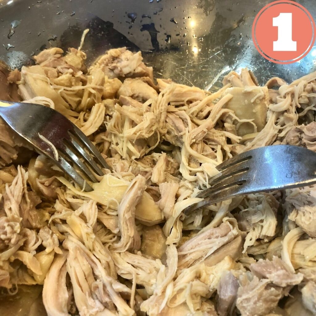 Two forks shredding chicken in a stainless steel bowl
