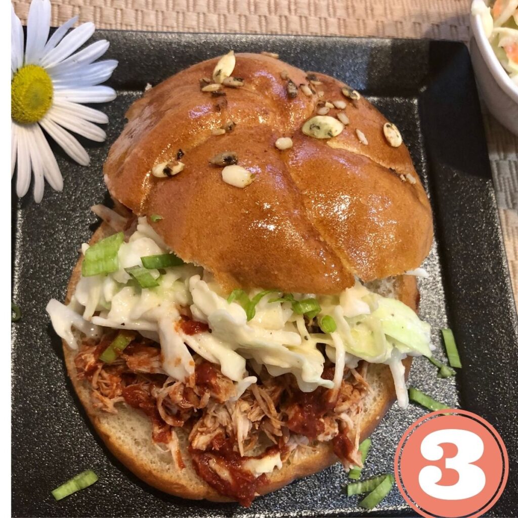 Buffalo chicken sandwich with coleslaw on a black plate with a daisy flower