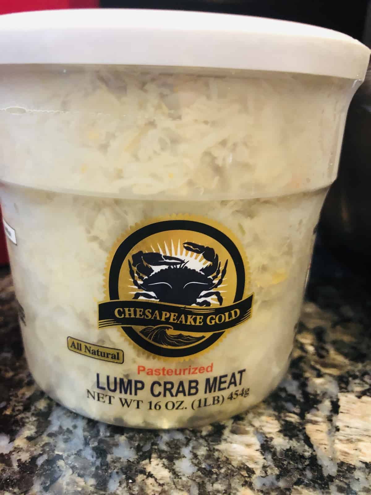 A container of Lump Crabmeat for the crab cakes sitting on a black granite countertop