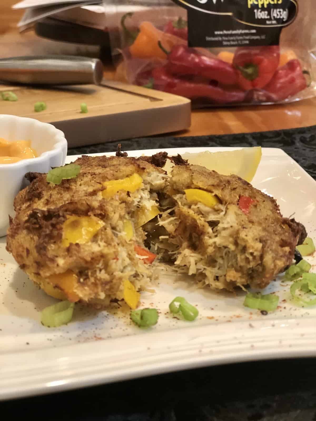 Air Fryer Crab Cake on a white plate with a lemon wedge and dip and a bag of peppers in the background