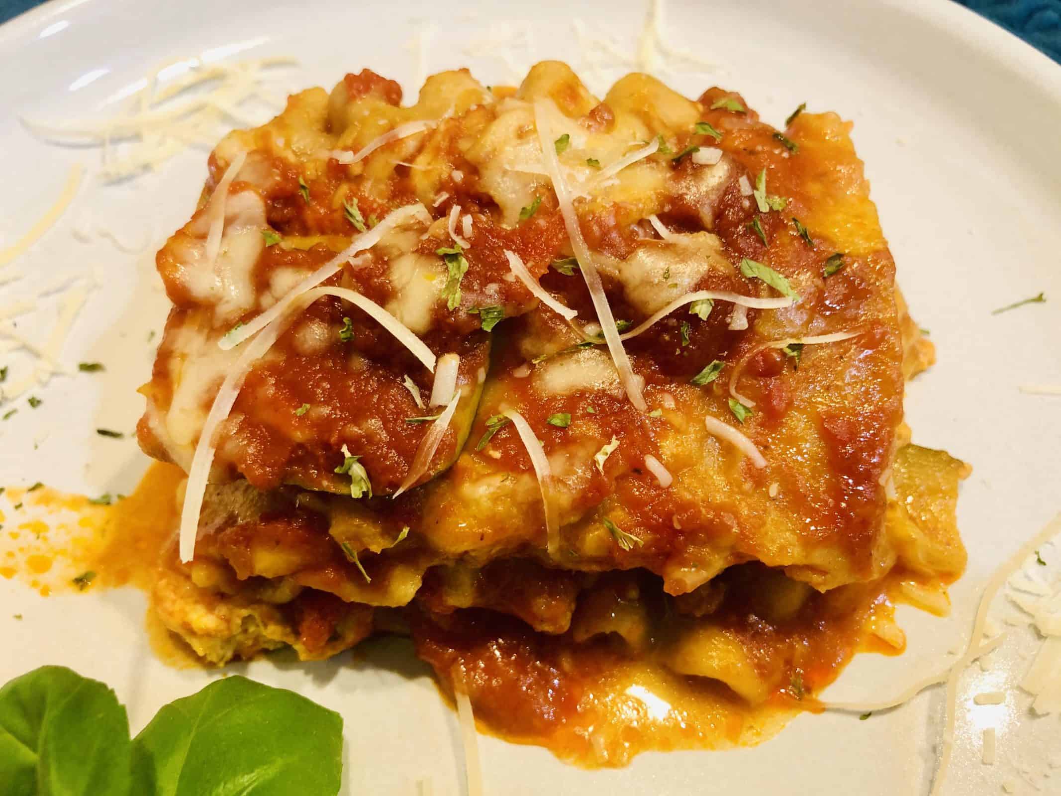 A serving of crockpot lasagna on a white plate with grated cheese and basil