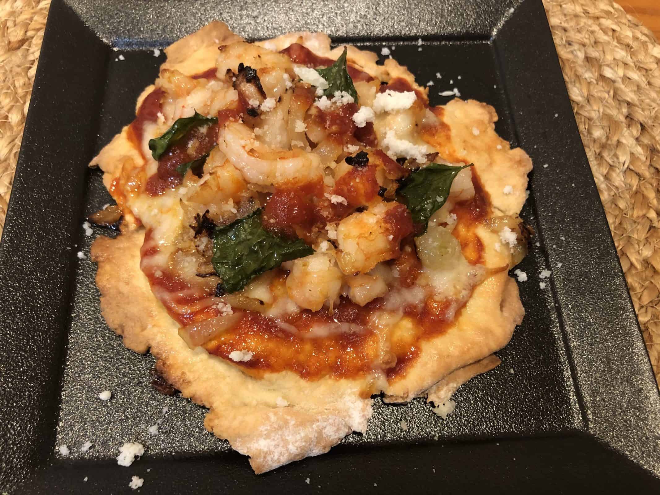 Homemade Artisan Style Shrimp Pizza on a black plate on a wicker placemat