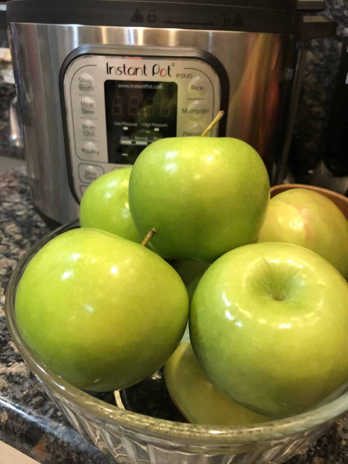 A bowl of Granny Smith Apples and an instant pot sitting on a granite kitchen counter