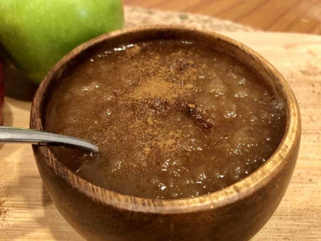 Healthy Homemade Applesauce in a wooden bowl with cinnamon sprinkled on top with a spoon dipped in the applesauce