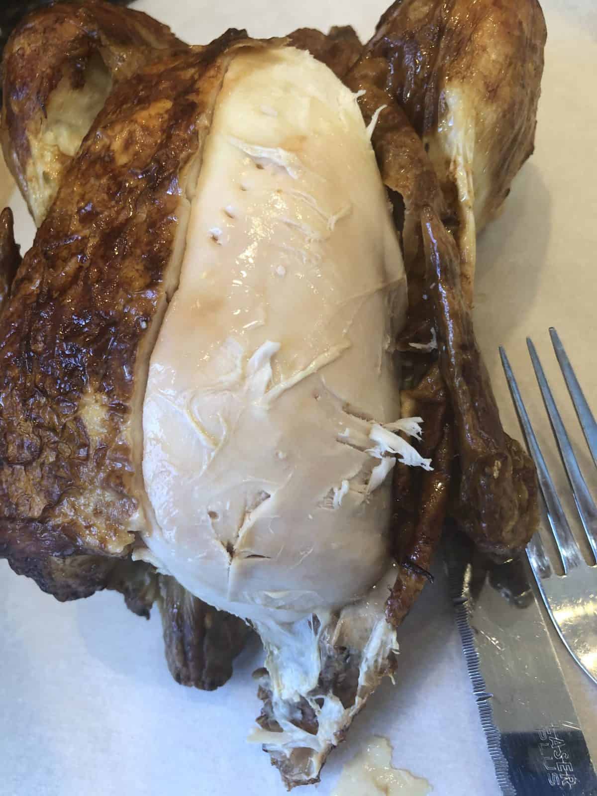 Rotisserie Chicken on a white plate with a fork and the skin peeled back