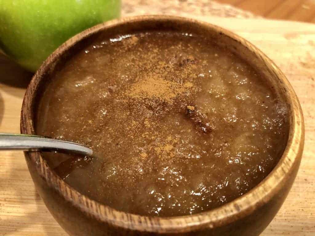 homemade healthy unsweetened applesauce in a wooden bowl with a spoon and a green apple