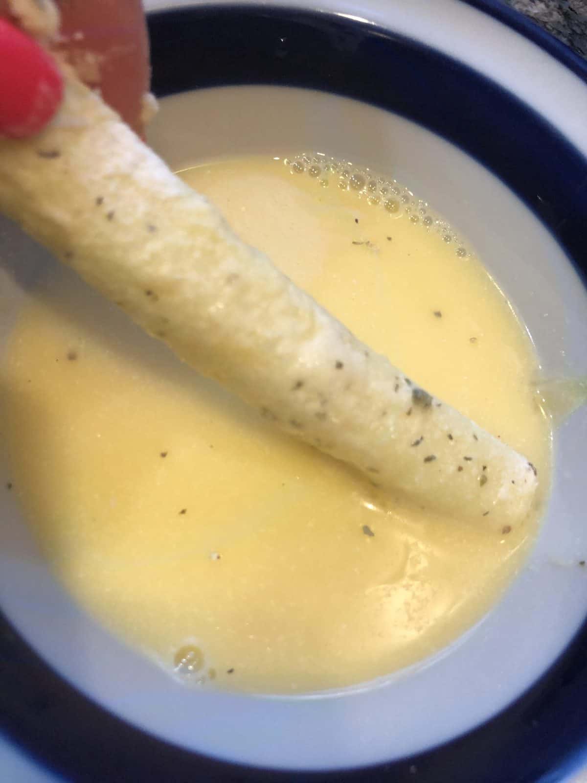 Battering cheese sticks in coconut flour and egg in a white and blue bowl