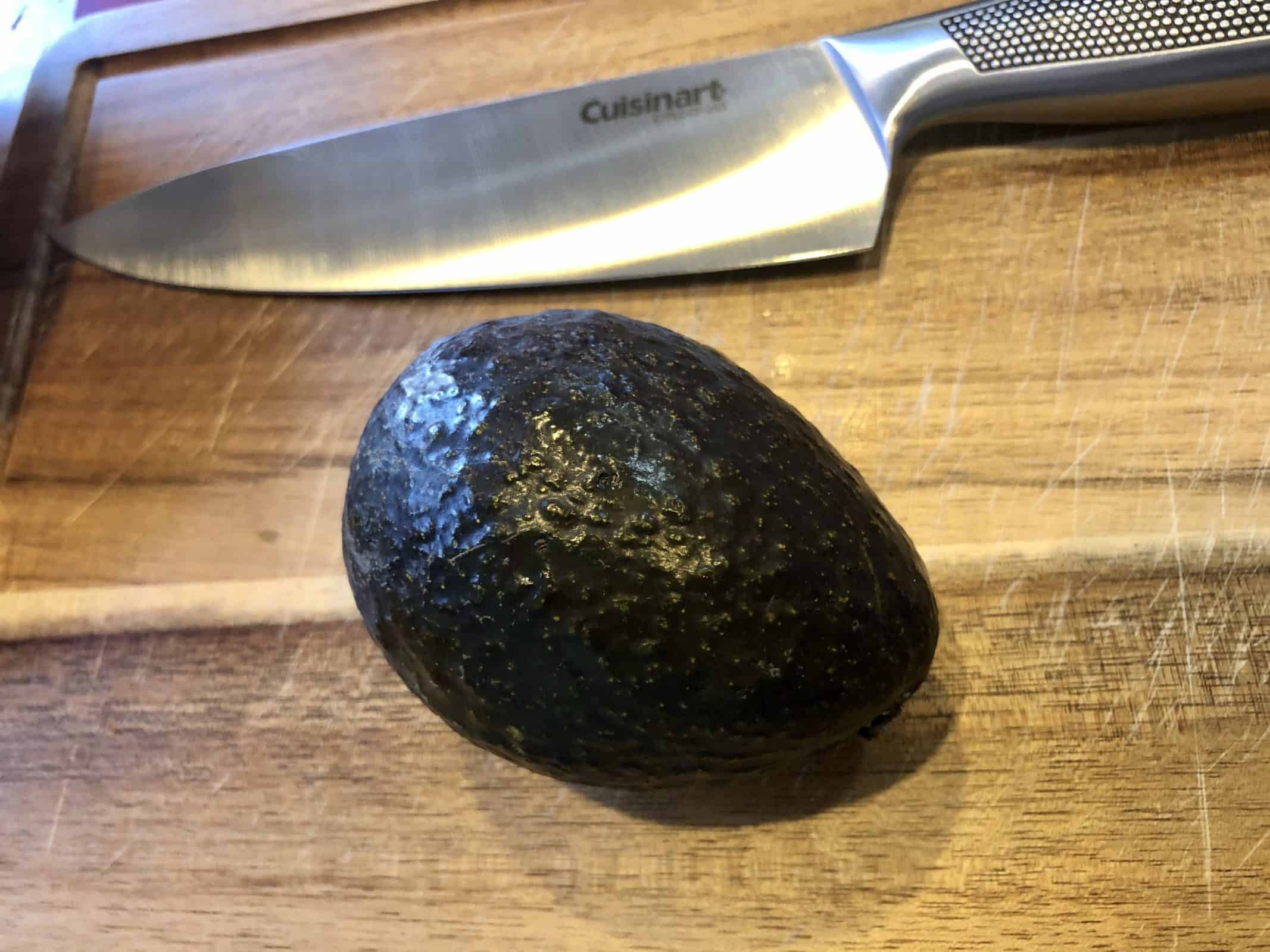 Fresh Avocado sitting on a wooden cutting board with a stainless steel knife
