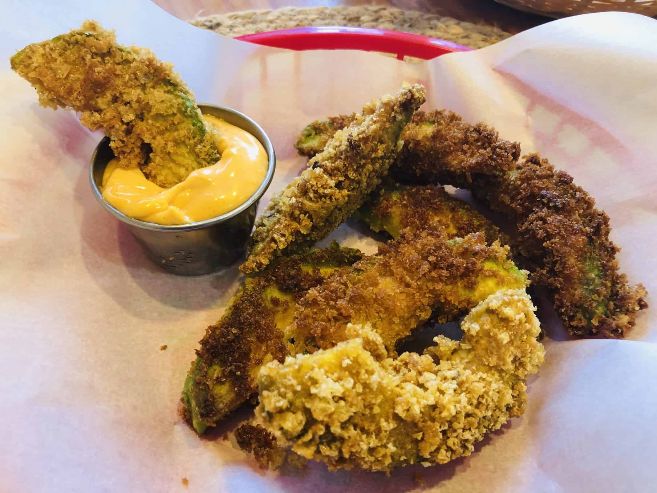 Fresh Baked Avocado Fries in a red basket with parchment paper and a single avocado fry dipped in cheese sauce