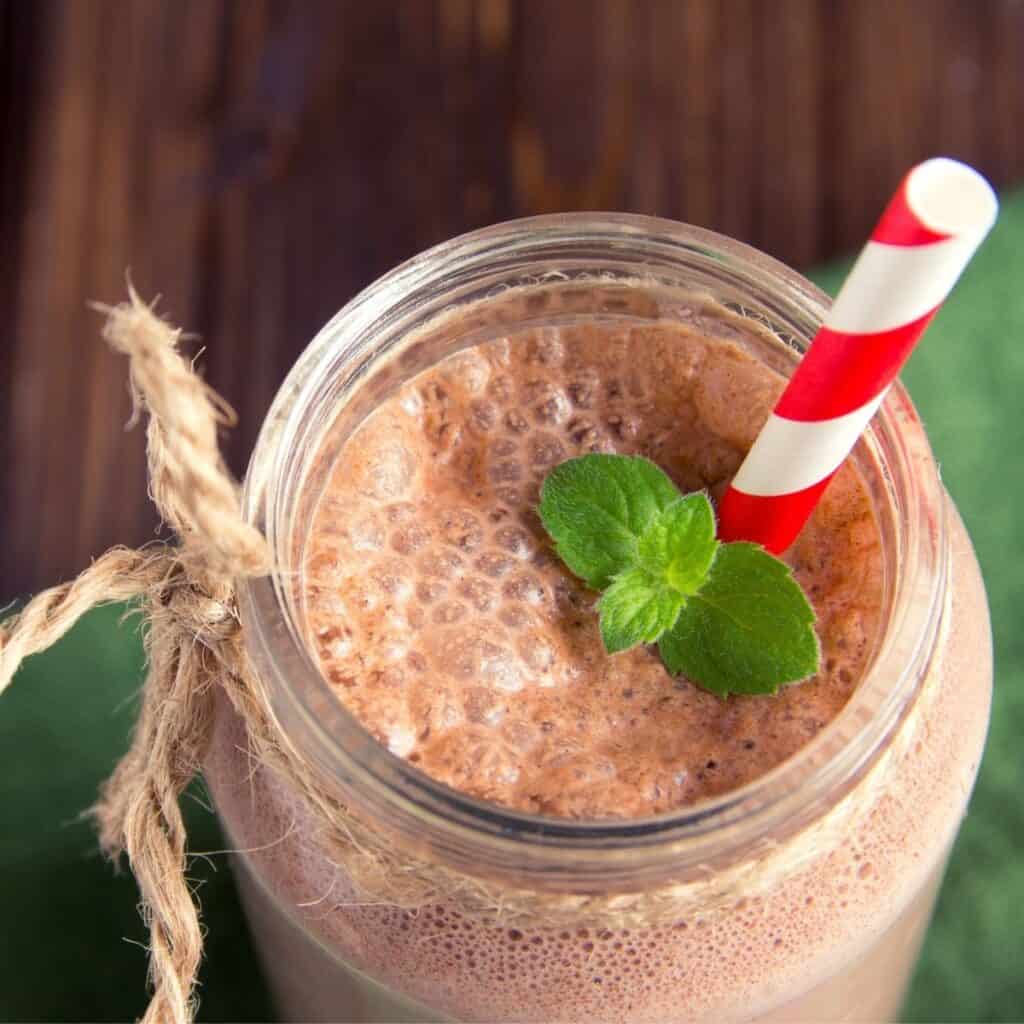 Low carb chocolate milkshake in a mason jar with a red and white striped straw and a sprig of mint