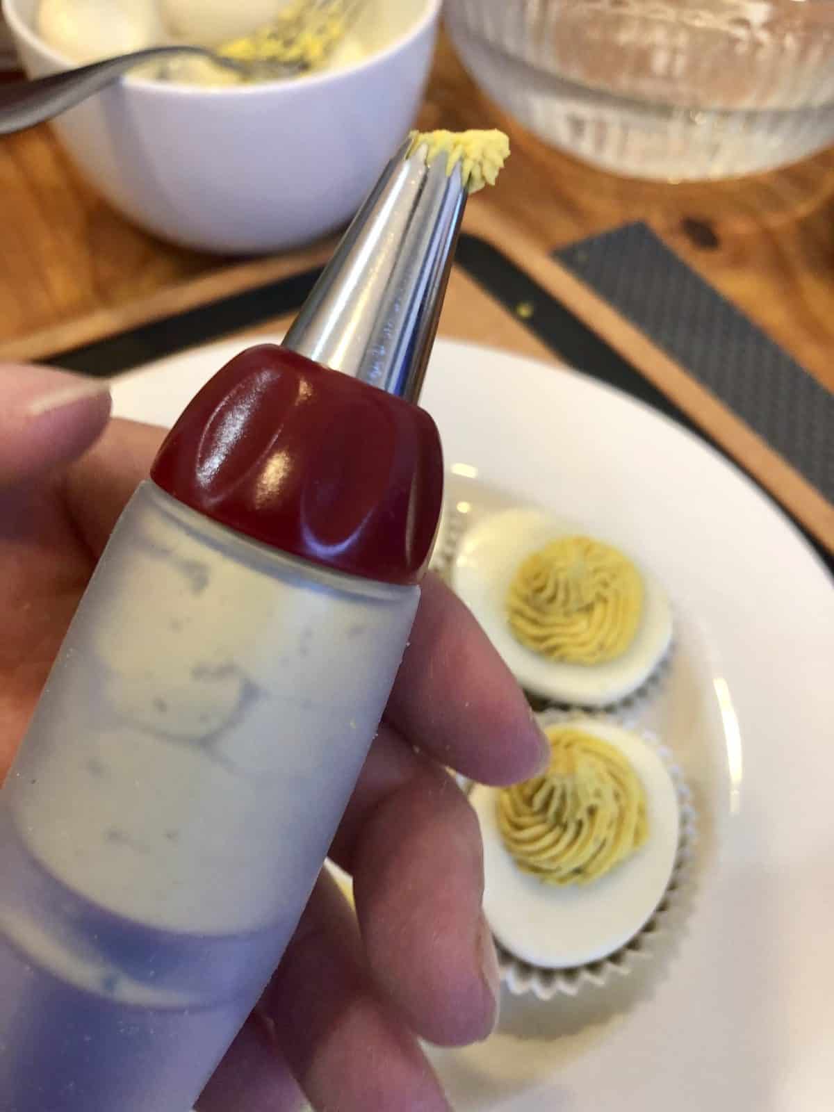 a hand holding cake decorator with whipped egg yolk over a plate of deviled eggs