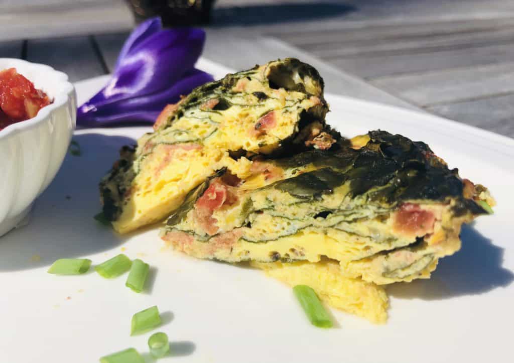 Spinach Egg Tomato Frittata on a white plate with diced scallions and salsa and a purple flower