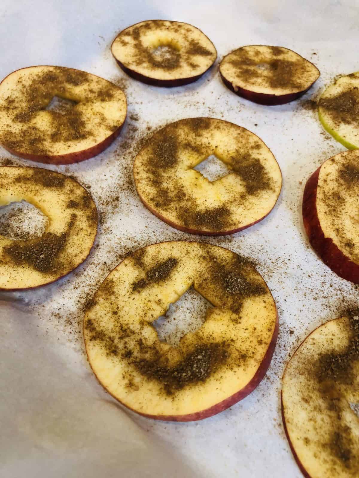 Apple Slices on Parchment Paper sprinkled with cinnamon ready to be Baked