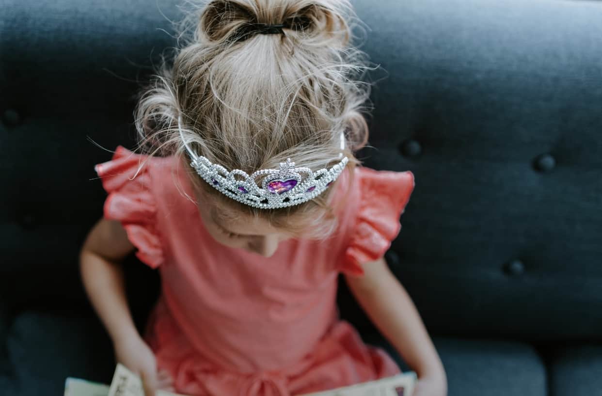 A little blonde girl with a princess crown on her head wearing a pink dress