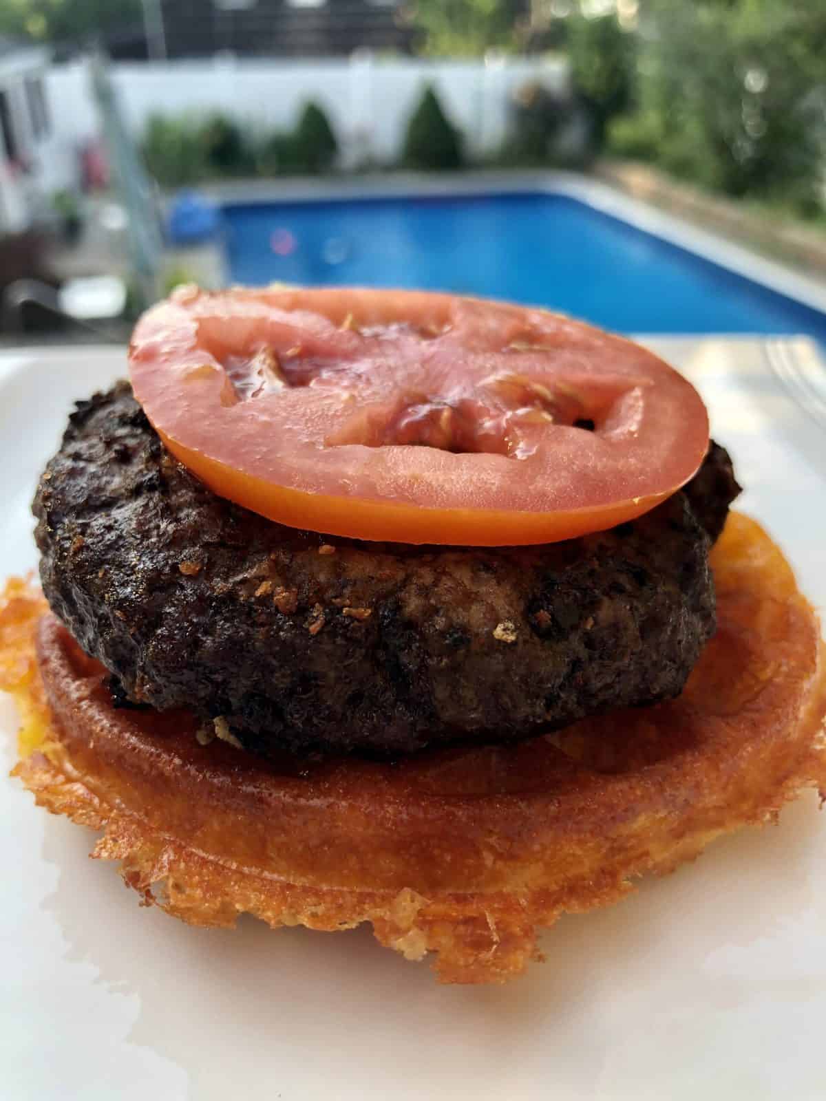 Chaffle Burger with a slice of tomato on top in front of an unground pool