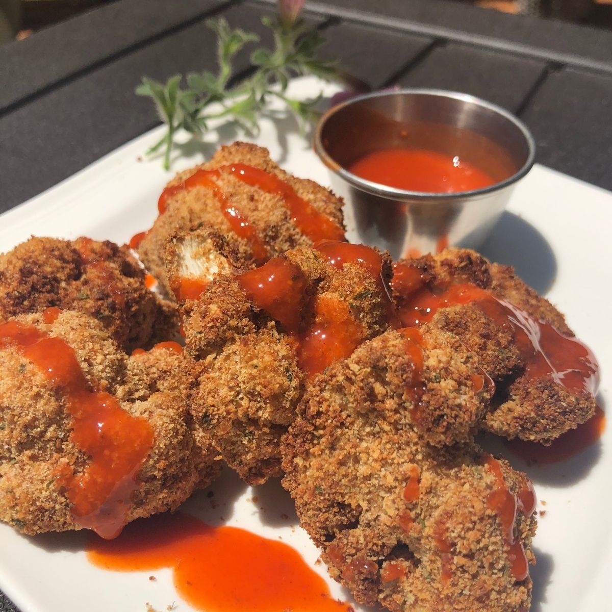 Air Fried Cauliflower Fritters on a white plate drizzled with hot sauce with a side of hot sauce in a stainless steel cup