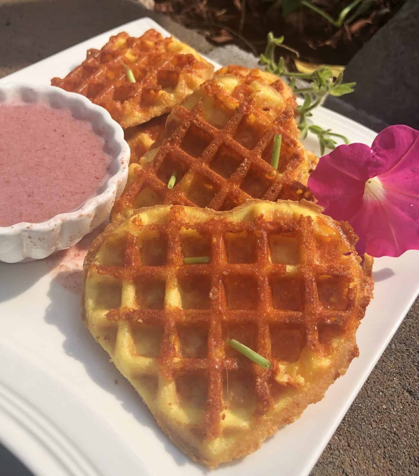 Heart shaped keto chaffles on a white plate with a side of strawberry dipping sauce