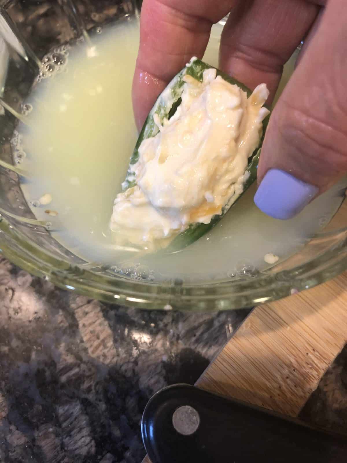 Dipping Stuffed Jalapeno in Egg Whites in a clear glass bowl on a black granite counter top