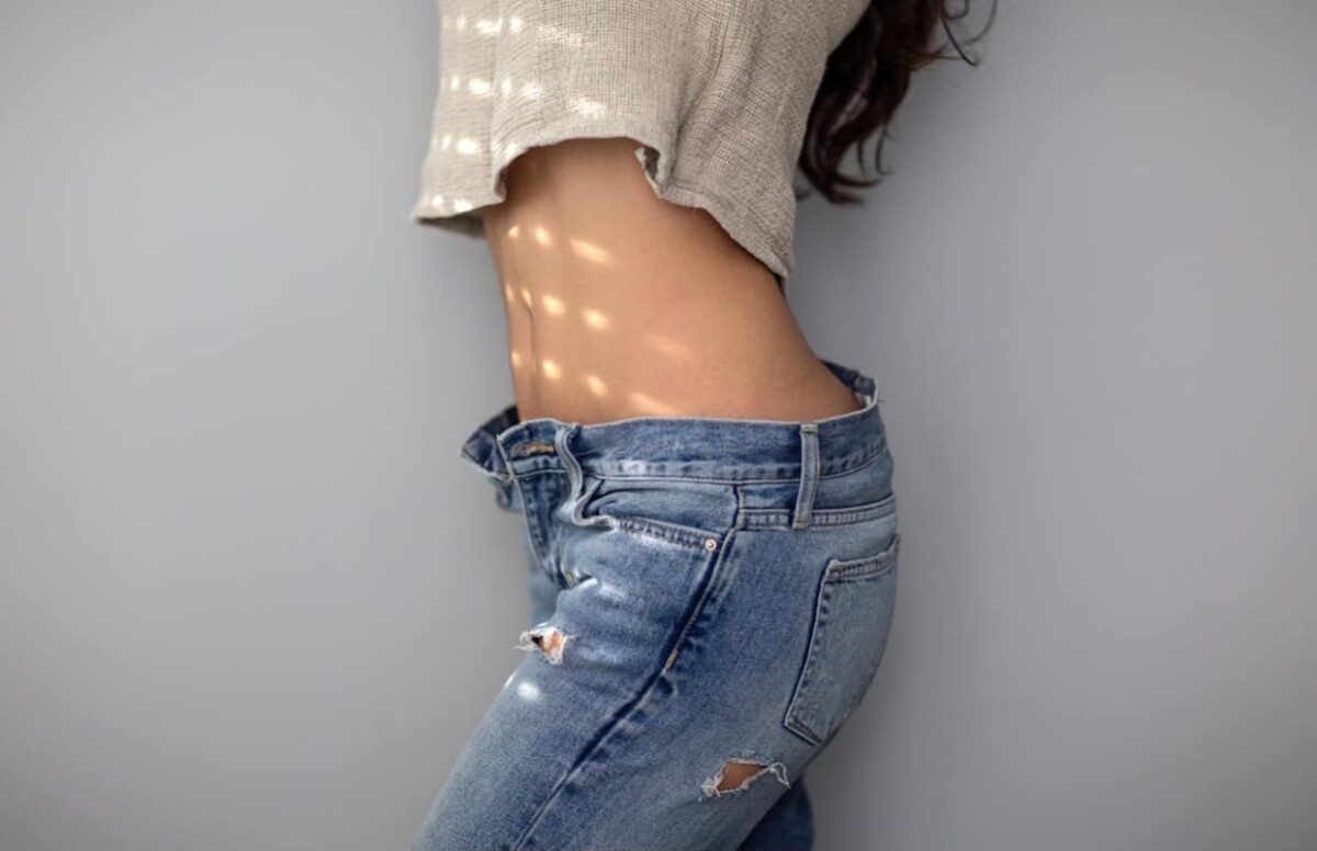 Female with flat tummy wearing ripped up blue jeans and a tan crop top sweater