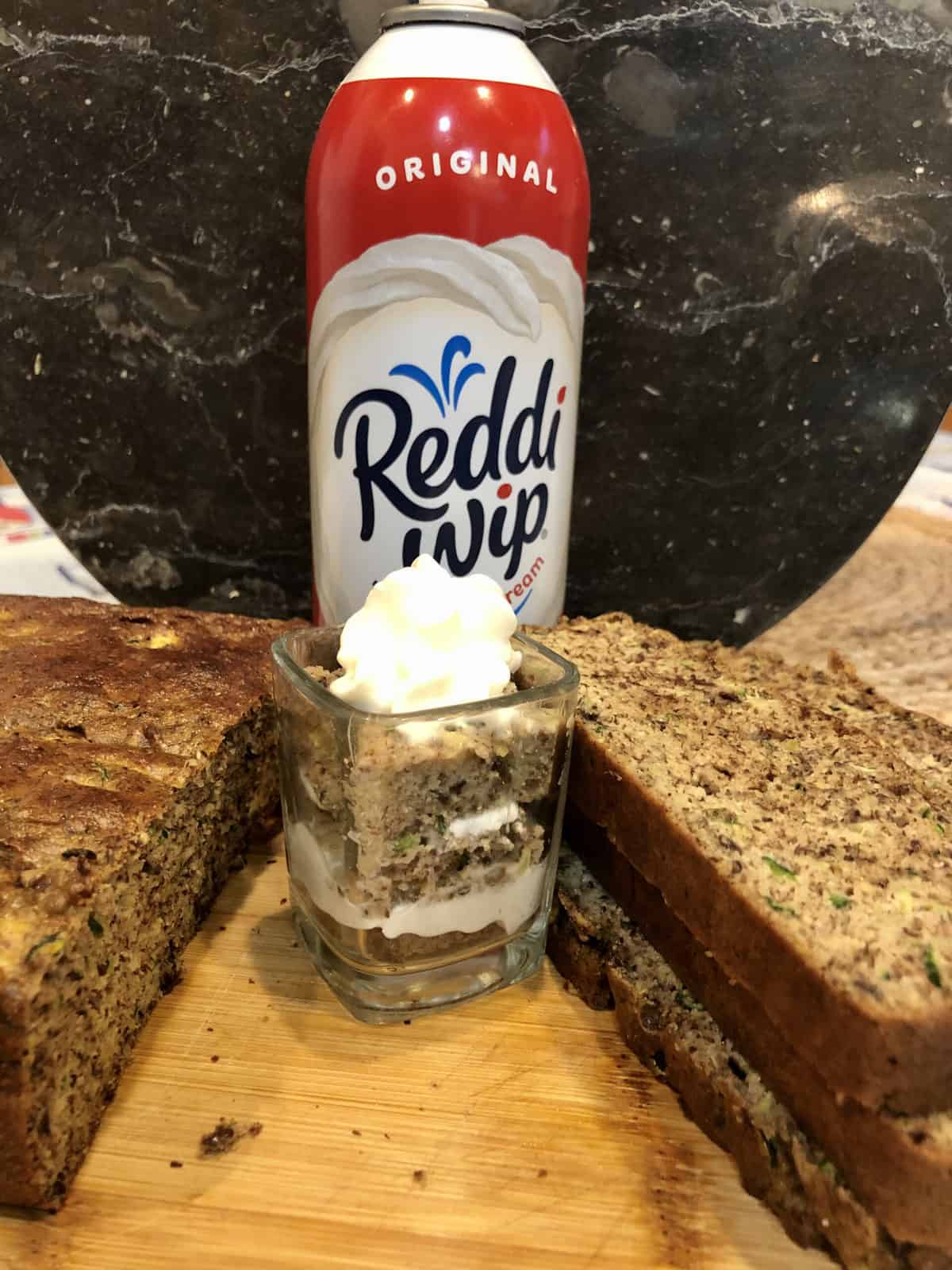 Sliced Zucchini Bread with a shot glass filled with layers of zucchini bread and whipped cream and a can of Reddi Dip
