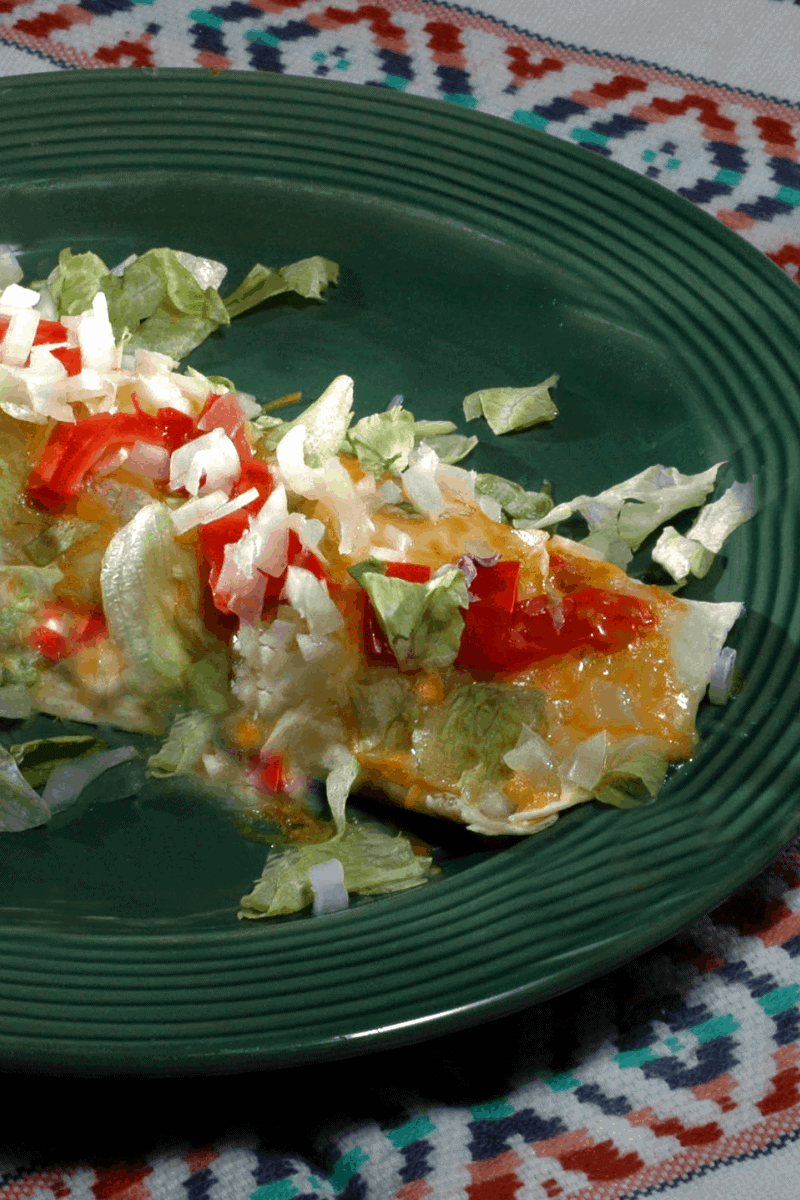 Vegetable Enchilada topped with shredded lettuce and cheese and red peppers on a green plate
